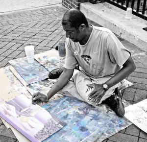 Homeless man in Baltimore, Md. painting on cardboard boxes to earn money. (James Held/Submitted Photo)