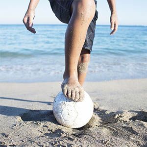 A child holds his foot on a soccer ball at the beach