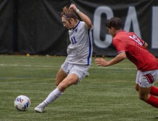 A Cabrini men's soccer player in their home white uniforms lines up to strike the ball with an opposing defender right next to him.