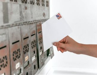 Hand placing a mail in ballot inside a mailbox