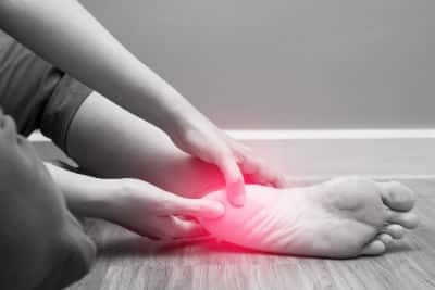 A woman holds her sore heel which is shown in red