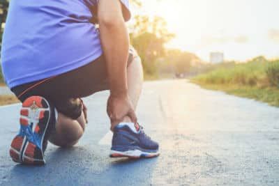 A man kneeling down to hold his sore heel while running