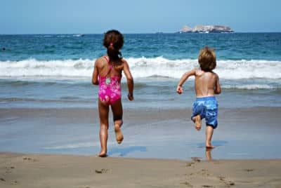 Two children are running towards the water on the beach and having fun
