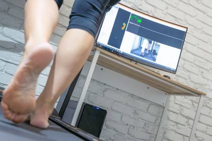 The legs and feet of someone walking on a treadmill with a screen in the background