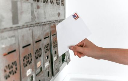 Hand placing a mail in ballot inside a mailbox