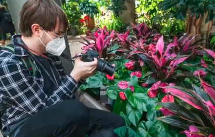 Male student kneeling with camera taking a photo of flowers at Longwood Gardens