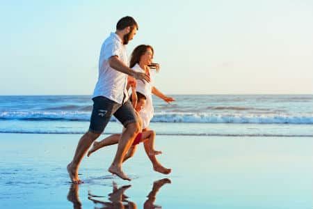 A family running barefoot on the beach