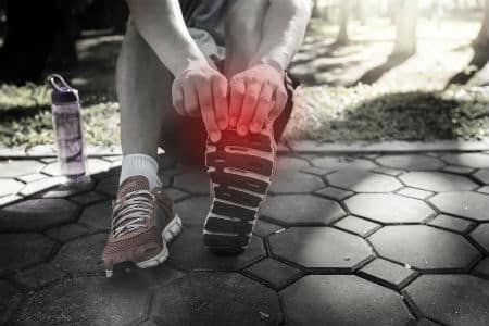 A runner holds their toe on the side of the road because it is sore