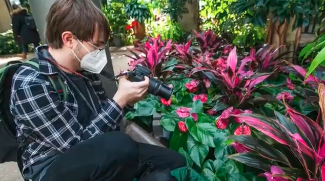 Male student kneeling with camera taking a photo of flowers at Longwood Gardens