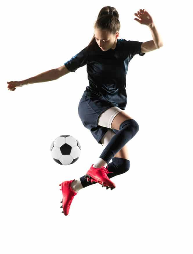 A young woman leaps in the air to kick a soccer ball