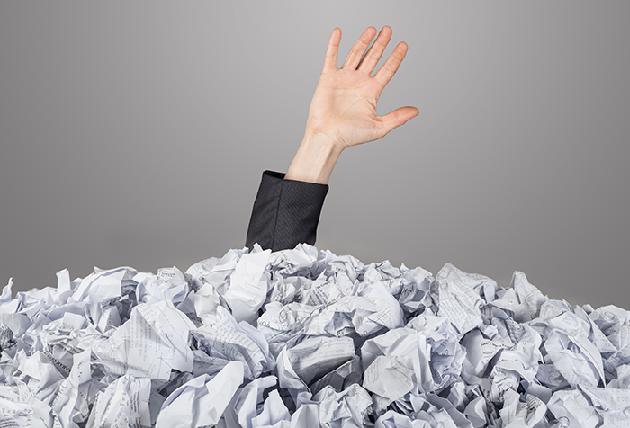 hand reaching out from pile of paper containing an overload of information