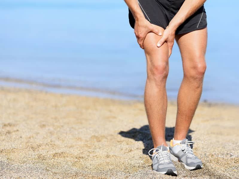 A man clutches his right thigh on the beach