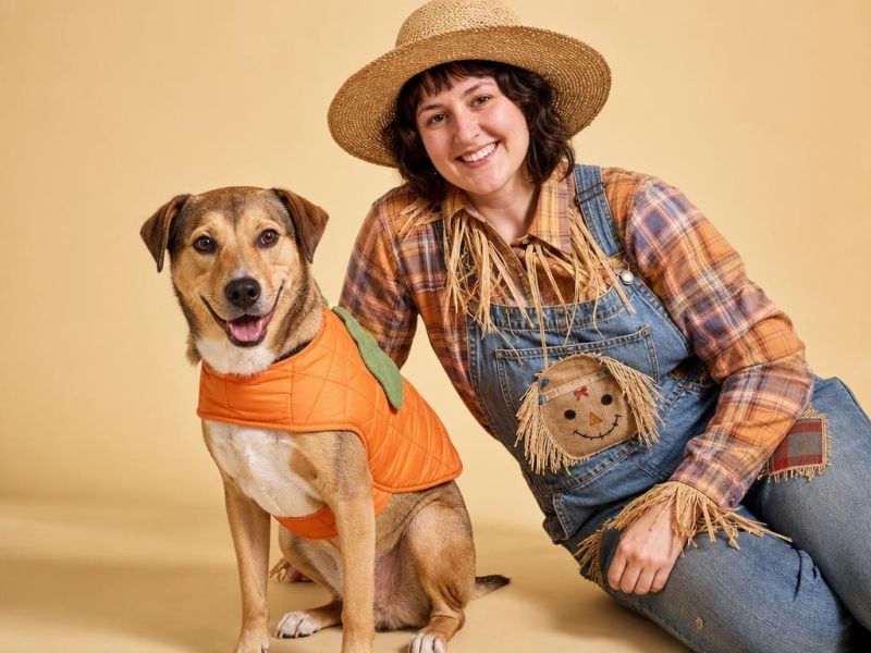 Un perro con chaleco de calabaza y su dueña vestida de espantapájaros