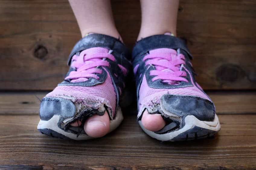 Worn out shoes with the big toes poking out of the shoes on a child
